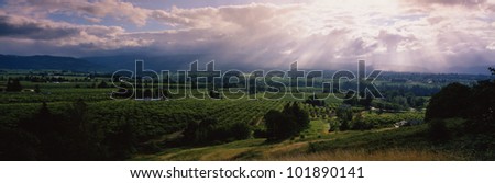 This is a green valley with houses and farms scattered throughout. The sun is projecting rays down over the valley through the white clouds.