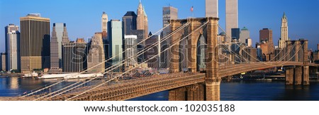 This is a close up of the Brooklyn Bridge over the East River. The Manhattan skyline is behind it at sunrise.