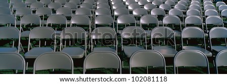These are empty, grey folding chairs awaiting a crowd to attend a Graduation Ceremony. They are neatly set up in rows side by side.