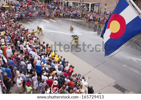 Colorado flag hangs as men dressed in yellow firemen slickers and firehoses have annual Waterfight on July 4, Main Street, Ouray, CO, sponsored by Ouray Fire Department