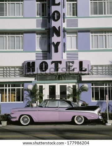 This is the Colony Hotel on the strip of South Beach Miami. There is a purple and black vintage car parked in front of the hotel.