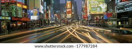 This is Times Square at night. There are streaked lights from the cars traveling through the square. There are neon lights from the billboards as well as signs.