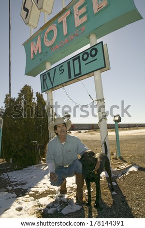 Cowboy and his dog kneel down in front of the Sands Motel Sign with RV Parking for $10, located at the intersection of Route 54 & 380 in Carrizozo, New Mexico