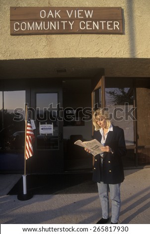 Woman voter reading election pamphlet at the entrance to a polling place, CA