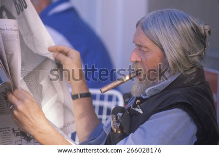 An older man reading a newspaper and smoking a cigar
