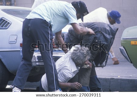 Fallen homeless man in city street getting help, Los Angeles, California