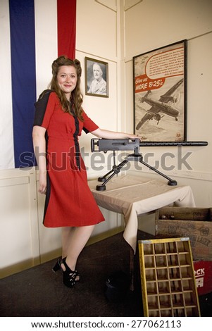 Attractive woman in red vintage 1940s red dress with knee up near World War II machine gun and a poster, Mid-Atlantic Air Museum World War II Weekend and Reenactment in Reading, PA held June 18, 2008