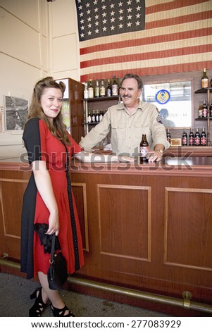 Attractive 1940s woman in red dress in front of World War II-style bar with bartender at the Mid-Atlantic Air Museum World War II Weekend and Reenactment in Reading, PA held June 18, 2008