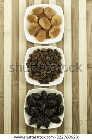 Dried fruits in white bowls on wooden table photographed from above. Photo is sepia toned and little noise was added.