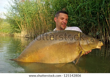 Carp fishing scene. Fisherman holding a large mirror carp