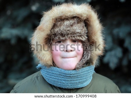 boy with a smile cute cheeks pink winter hat hood in the background of blue spruce