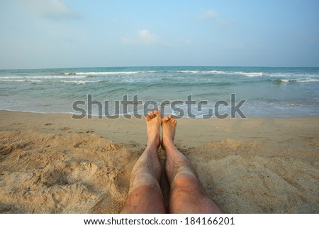 male legs on beach.Legs man lying on the beach shore of the Indian Ocean. Bay of Bengal Passikuda beach.