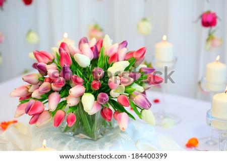 big multicolored bouquet of tulips on a wedding table.Candle flame yellow flame. Rose buds hanging decoration