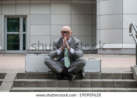 a man with a shaved head in a suit sitting on the steps of the office