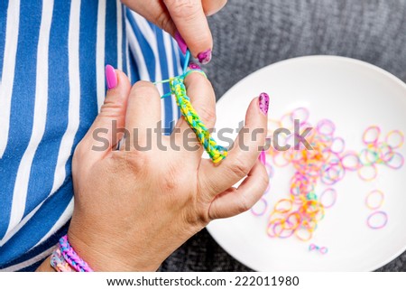 Women with colorful nails making a rubber loom bracelet with a hook . Hands close up. Young new modern fashion concept.