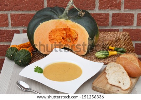 a plate of pumpkin soup, bread and a pumpkin on a table
