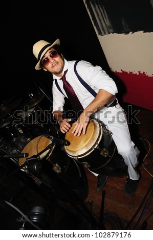Portrait of young male percussionist playing cuban drums against black background