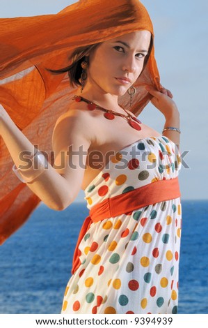 Fashion model holding orange cloth against ocean background