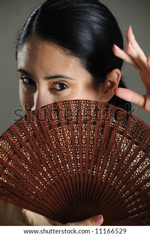 Portrait of passionate flamenco dancer girl covering her face with traditional fan