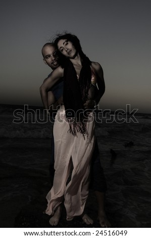 Low key portrait of young couple standing against ocean background at sunset