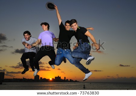 Group of four young males jumping against sunset sky background with happy expression