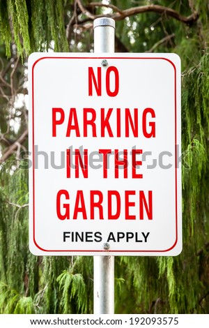 Red, white and black sign against background of green trees stating: No Parking in the Garden, Fines Apply
