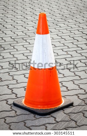 Orange, reflective white and black temporary movable traffic cone on grey paved street with lines of tires