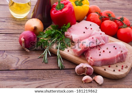 Raw meat for barbecue with fresh vegetables on wooden surface. Food, meat raw steak, beef steak bbq, tomatoes, peppers, spices for cooking meat. Free space for text.