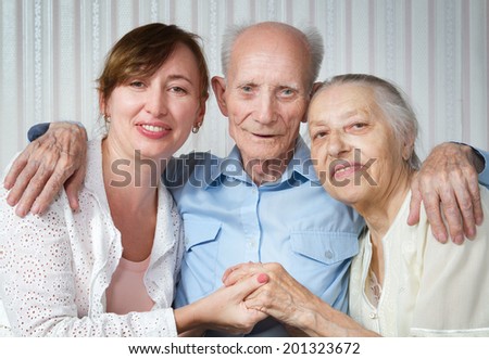 Senior man, woman with their caregiver at home. Concept of health care for elderly old people, disabled. Happy family. Portrait of elderly parents and adult daughter happily looking at the camera.