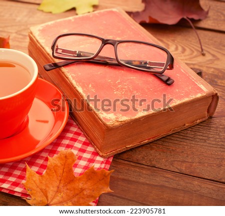 Autumn leaves, book and cup of tea on wooden table. square