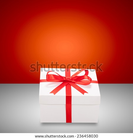 Beautiful white gift box with red ribbon and bow on table. Holiday presents.