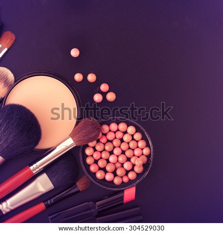 various makeup products on black texture background. Selective focus, color toning.