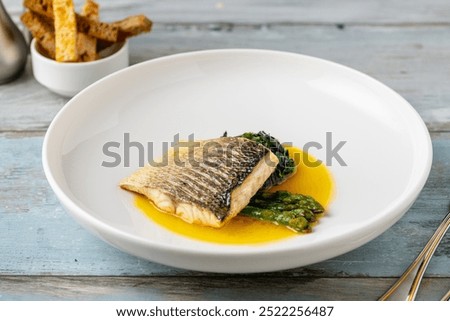 Foto Bild Zubereitung von Bass-Fischfilets in mediterraner Sauce mit Tomaten, Oliven und Kapern in einer Backform auf rustikalem Holzgrund mit Zutaten. Ansicht von oben