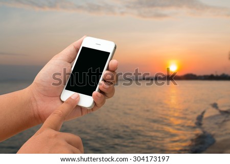 Mobile men and touchscreen smartphone, tablet, mobile phone over blurred beautiful clear blue sky and beach background. Abstract background for online work on the holiday.