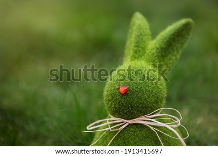 Close up Easter bunny rabbit statuette and basket with easter eggs on the green grass lawn background. Easter egg hunt in the garden. Selective focus, copy space