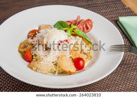 Classical Caesar salad with  sliced chiken meat, grilled bacon, lettuce leaves, crackers and cherry tomatoes decorated with basil and parmesan  served in white round  plate
