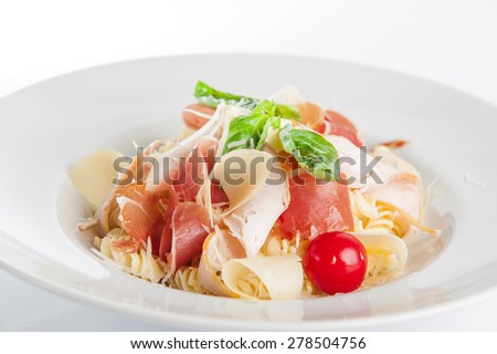 Close up  Plate of meat Pasta with ham and  prosciutto slices decoratred with cherry tomatos, parmesan cheese and basil on the white plate isolated