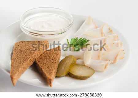 Close up Traditional Russian / Ukrainian appetizer for vodka: salted pork fat / bacon, slices of rye bread and pickled cucumbers with sauce on the white plate isolated