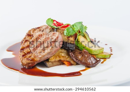 Restaurant serves meat steak with stewed vegetables and sauce: zucchini, eggplant, carrots, mushrooms, decorated with herbs and spices on white plate isolated