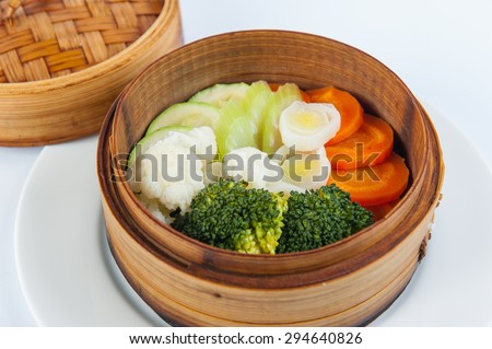 Close up Portion of steamed vegetables: broccoli, cauliflower, zucchini, celery, carrots in a wood tray on the white background isolated