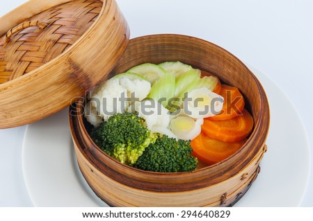 Close up Portion of steamed vegetables: broccoli, cauliflower, zucchini, celery, carrots in a wood tray on the white background isolated