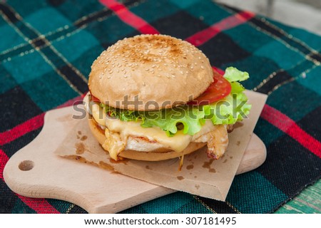 Sreet food  - burger with grilled chicken fillet, cheese and vegetables on wooden board close up selective focus
