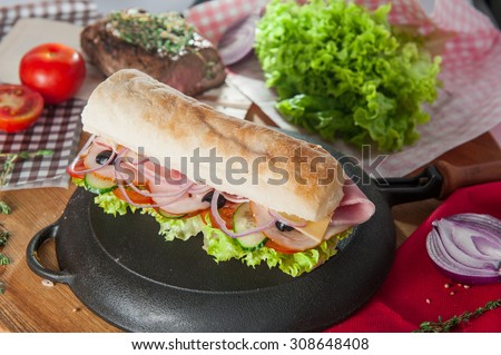 Close up Fresh sandwich with wheat bun, ham, bacon and vegetables in a pan on the table with colourfull ingredients