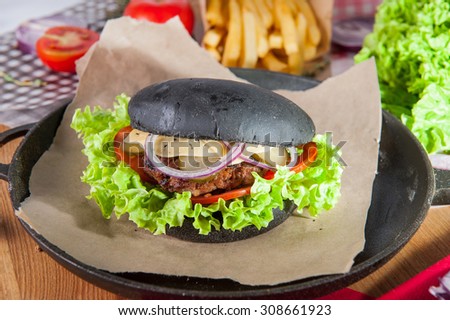 Close up Modern black Burger with beef meat, cheese, lettuce and vegetables in the pan on the table arounded with  potato wedges fried and some ingredients