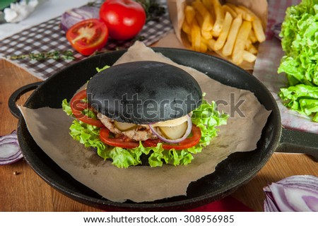 Close up  Black burger with pork chops, cheese and vegetables  in the pan on the table  arounded some ingredients