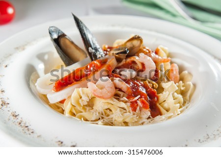 Plate of Italian Seafood Pasta with clam, shrimps, mussels and tomato sause decorated with shell mussel on the white plate on the served restaurant table