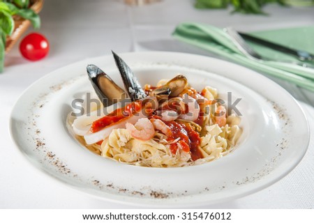 Plate of Italian Seafood Pasta with clam, shrimps, mussels and tomato sause decorated with shell mussel on the white plate on the served restaurant table