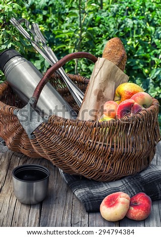 Straw basket with bread loaf,fruit and thermos for picnic on the background lawn .Photo tinted.Selective focus