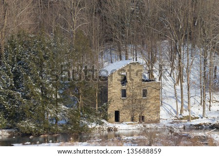 Old stone building on stream bank in winter