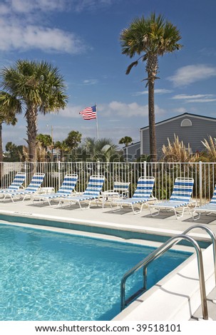 A view of a pool with palm trees and an American flag in the background.